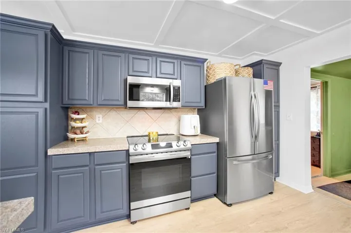 Kitchen featuring stainless steel appliances, backsplash, light wood-style floors, light countertops, and blue cabinetry