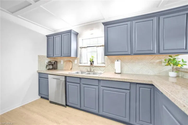 Kitchen with stainless steel dishwasher, a sink, light wood-style flooring, and tasteful backsplash