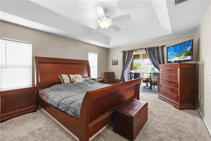 Bedroom featuring light carpet, ceiling fan, and a tray ceiling