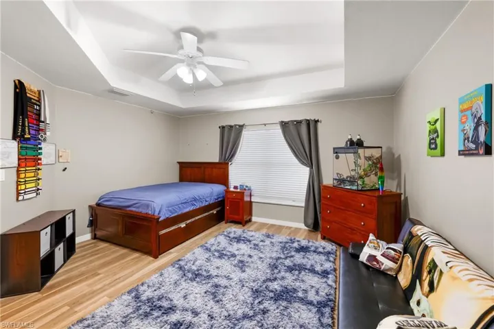 Bedroom with wood-type flooring, ceiling fan, and a tray ceiling
