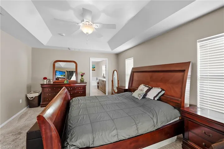 Carpeted bedroom with ceiling fan, ensuite bath, and a raised ceiling