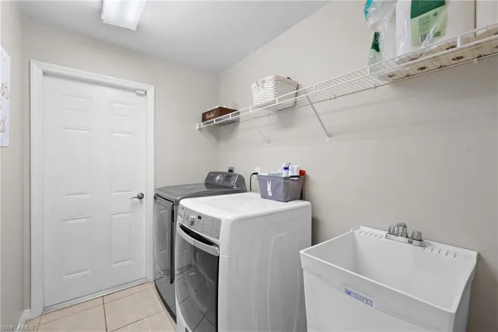 Washroom with sink, washing machine and clothes dryer, and light tile floors