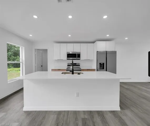Kitchen featuring an island with sink, stainless steel appliances, white cabinetry, recessed lighting, and light wood-style flooring