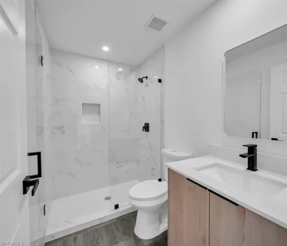 Full bath with vanity, a marble finish shower, and dark wood-style floors