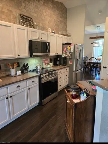 Kitchen with appliances with stainless steel finishes, hanging light fixtures, dark wood-type flooring, white cabinets, and backsplash