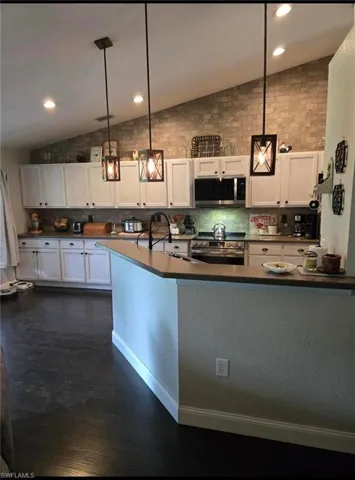 Kitchen with vaulted ceiling, white cabinetry, appliances with stainless steel finishes, and hanging light fixtures