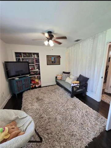 Living room with a textured ceiling, ceiling fan, and dark hardwood / wood-style flooring