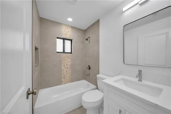 Bathroom featuring a white bathtub, tiled shower surround with accent band, built-in shower niche, and a window