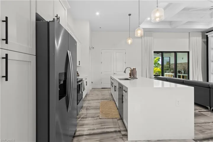 Kitchen with stainless steel appliances, white cabinets, beam ceiling, pendant lighting, and light stone countertops