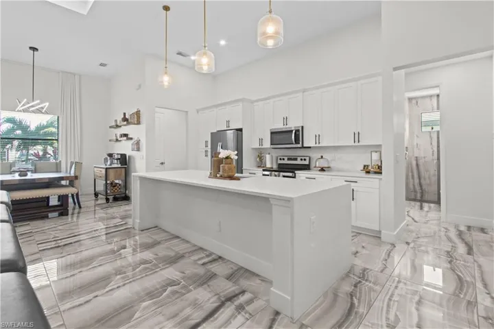 Kitchen featuring light marble finish flooring, white cabinetry, stainless steel appliances, healthy amount of natural light, and a towering ceiling