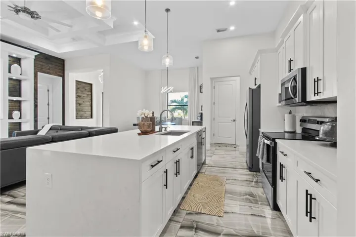 Kitchen with white cabinets, stainless steel appliances, open floor plan, pendant lighting, and a kitchen island with sink
