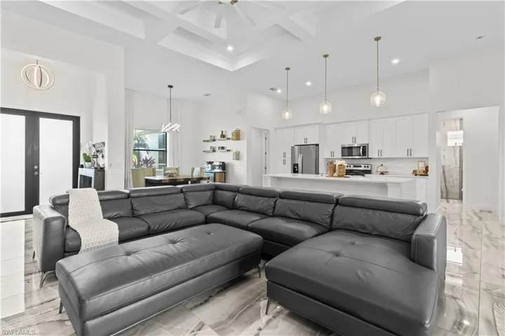 Living area with coffered ceiling, a high ceiling, beam ceiling, light marble finish floors, and a chandelier
