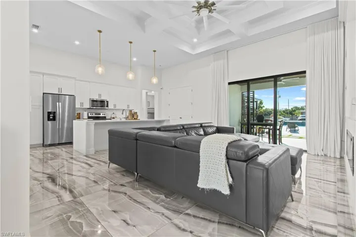 Living room with light marble finish floors, a towering ceiling, coffered ceiling, beam ceiling, and ceiling fan