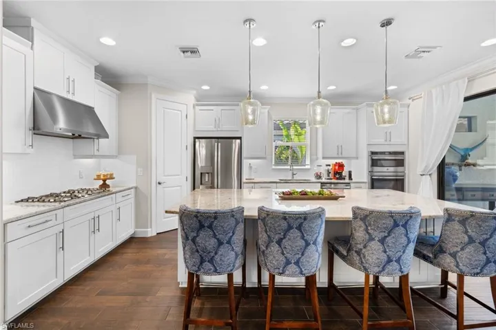 Kitchen with white cabinetry, light stone counters, ornamental molding, a kitchen bar, and stainless steel appliances