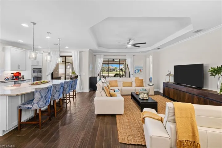 Living area featuring crown molding, a ceiling fan, dark wood-style flooring, a tray ceiling, and recessed lighting