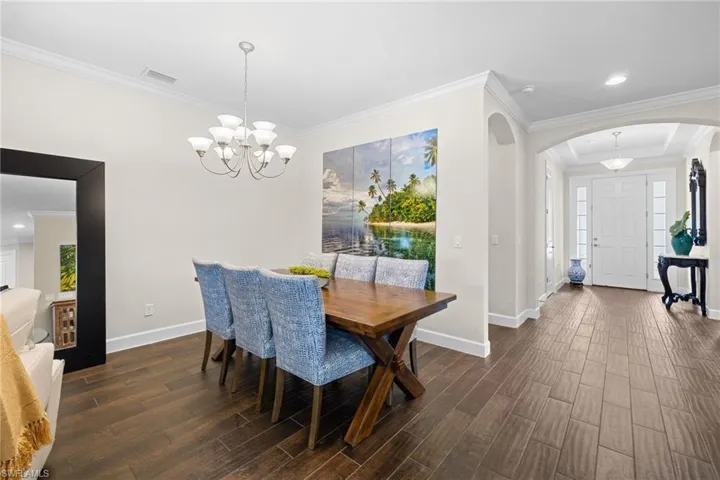 Dining room with arched walkways, ornamental molding, dark wood-type flooring, and hanging lights