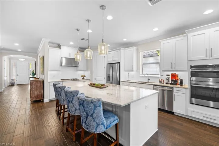 Kitchen featuring backsplash, arched walkways, a kitchen bar, crown molding, and white cabinetry