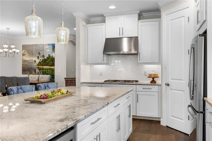 Kitchen with light stone counters, white cabinetry, crown molding, dark wood-style flooring, and freestanding refrigerator