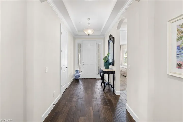 Foyer entrance featuring a raised ceiling, arched walkways, and dark wood finished floors