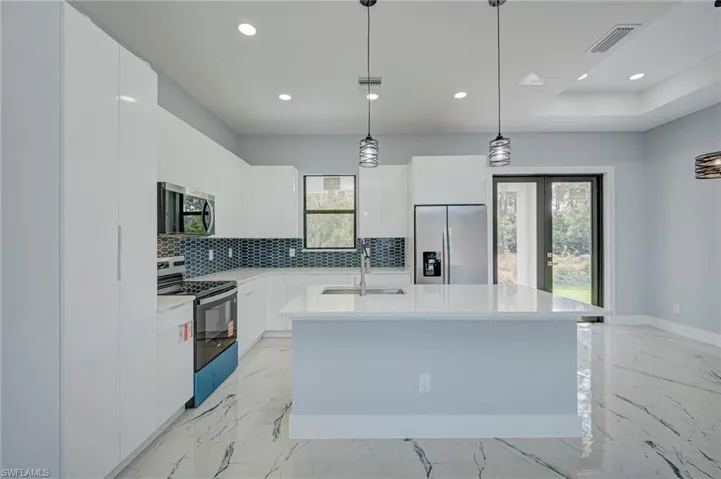 Kitchen featuring stainless steel appliances, light marble finish flooring, hanging light fixtures, and white cabinets