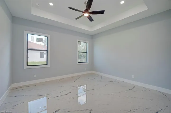 Empty room with light marble finish floors, healthy amount of natural light, a ceiling fan, recessed lighting, and a raised ceiling