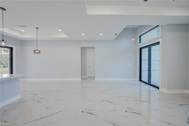 Empty room featuring a tray ceiling, light marble finish flooring, recessed lighting, and french doors