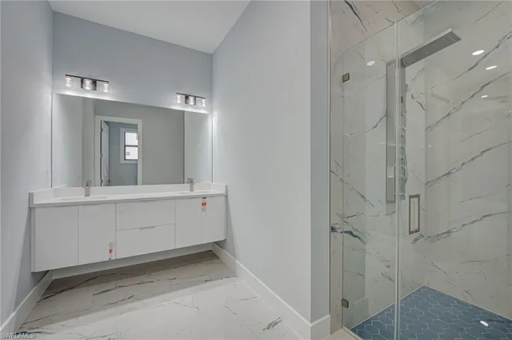 Full bathroom featuring a marble finish shower, double vanity, and light marble finish floors