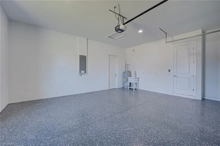 Garage featuring electric panel, electric water heater, recessed lighting, and a garage door opener