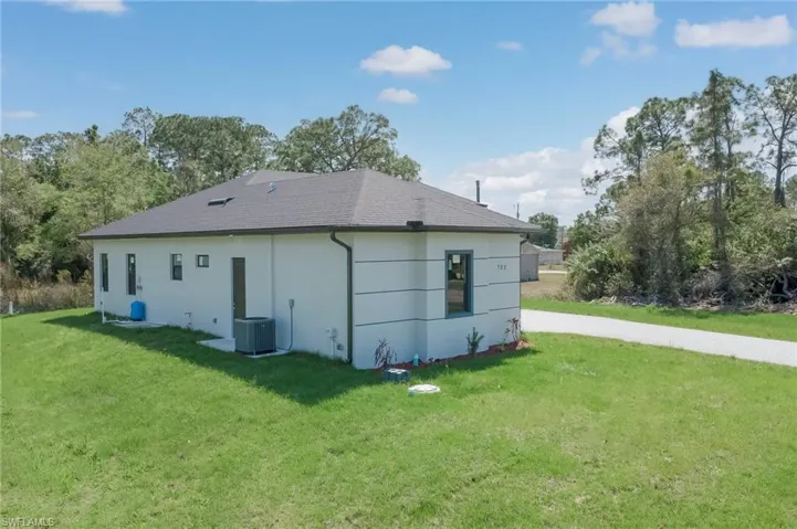Back of property with a lawn, roof with shingles, and stucco siding