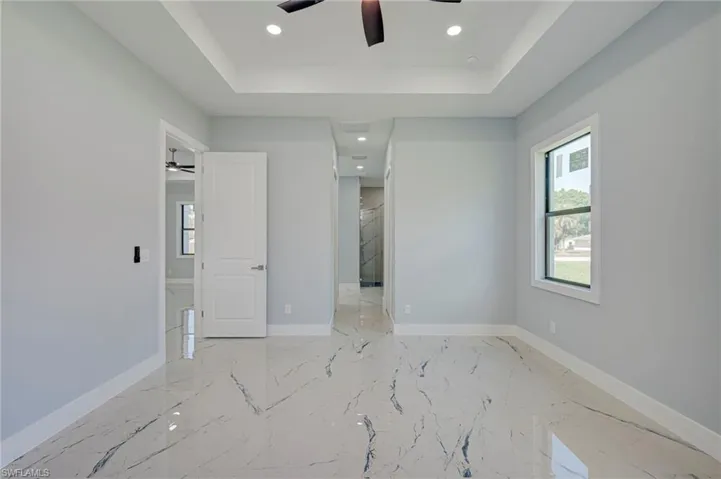 Unfurnished bedroom with recessed lighting, a tray ceiling, ceiling fan, and light marble finish floors