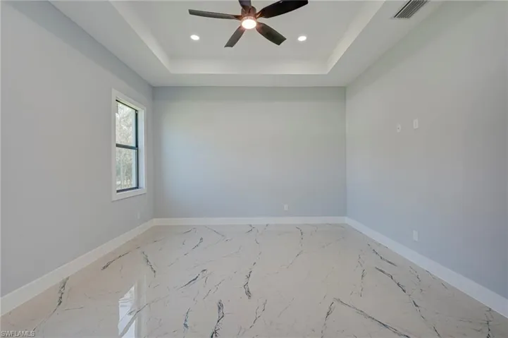 Empty room featuring a ceiling fan, a tray ceiling, recessed lighting, and light marble finish flooring