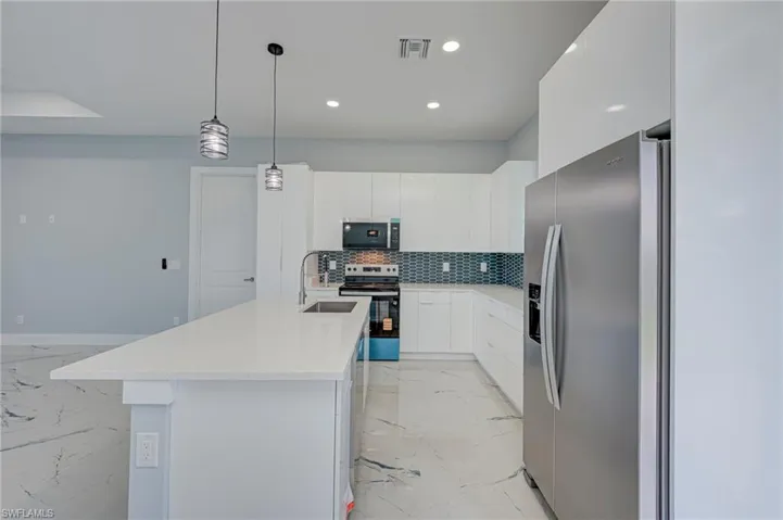 Kitchen with stainless steel appliances, light marble finish flooring, white cabinetry, and decorative light fixtures