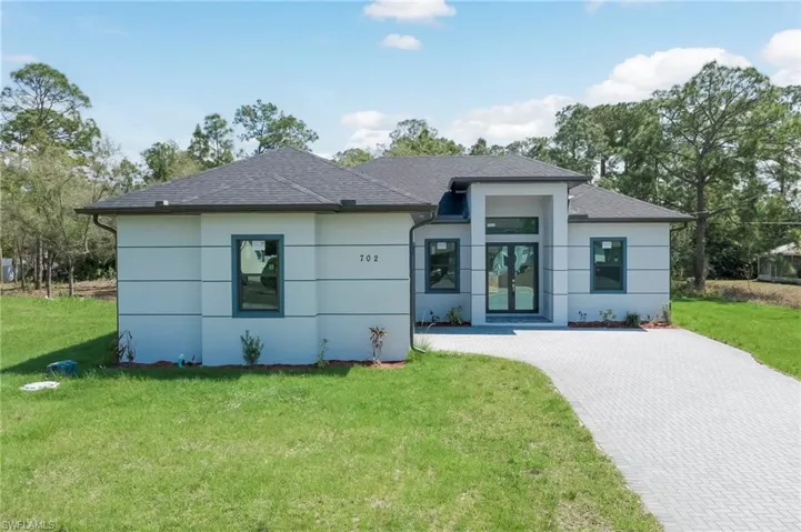 View of front of home featuring a front lawn, roof with shingles, decorative driveway, and stucco siding
