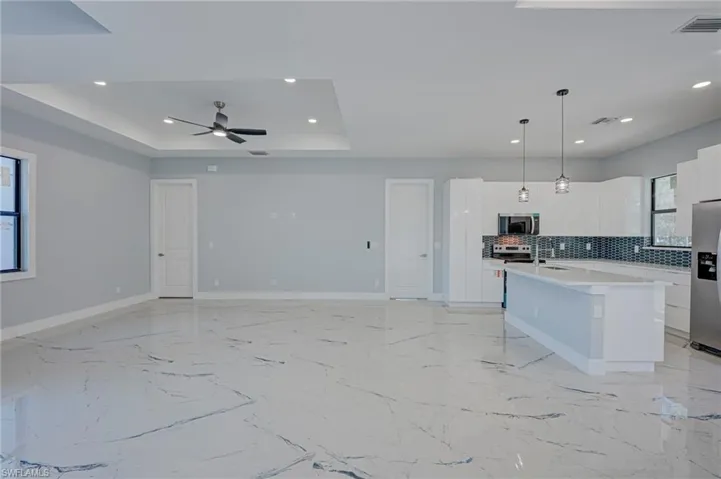 Kitchen featuring white cabinets, a center island with sink, hanging light fixtures, modern cabinets, and stainless steel appliances
