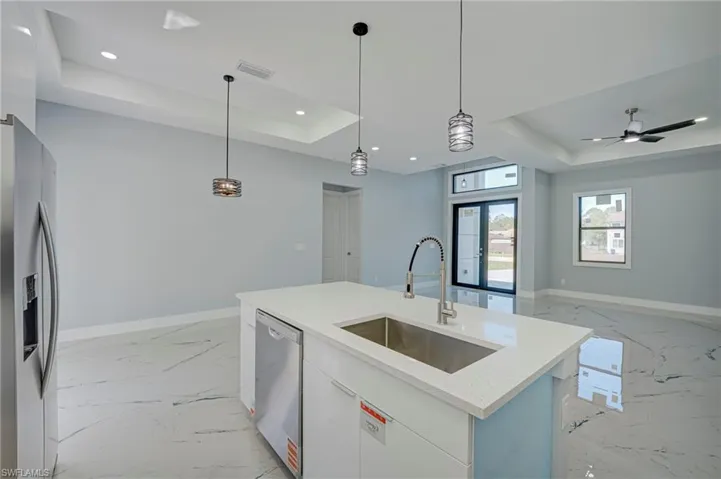 Kitchen with a raised ceiling, stainless steel appliances, white cabinetry, light stone counters, and open floor plan