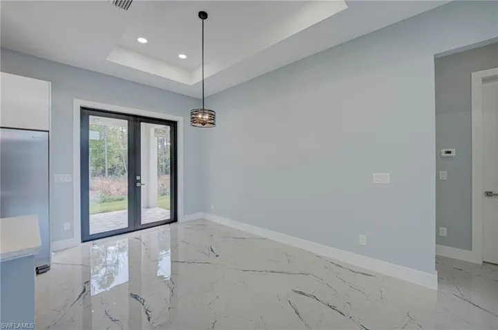 Unfurnished dining area with french doors, a raised ceiling, recessed lighting, and light marble finish flooring
