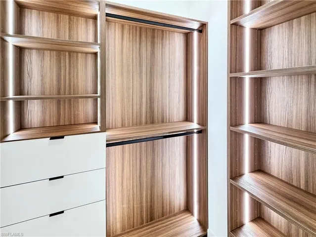 Built-in shelving with integrated lighting, wood-finish paneling, white drawer units with recessed pulls, and hanging rods