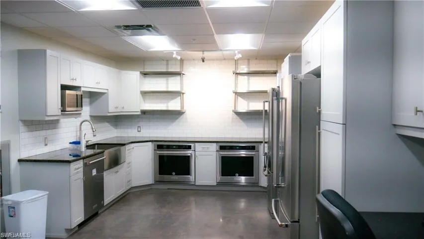 Kitchen with open shelves, a drop ceiling, a sink, appliances with stainless steel finishes, and backsplash