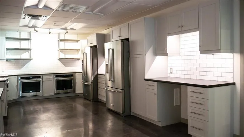 Kitchen with open shelves, backsplash, dark countertops, and appliances with stainless steel finishes