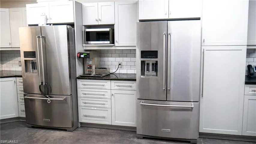 Kitchen featuring dark stone countertops, concrete floors, white cabinets, appliances with stainless steel finishes, and tasteful backsplash