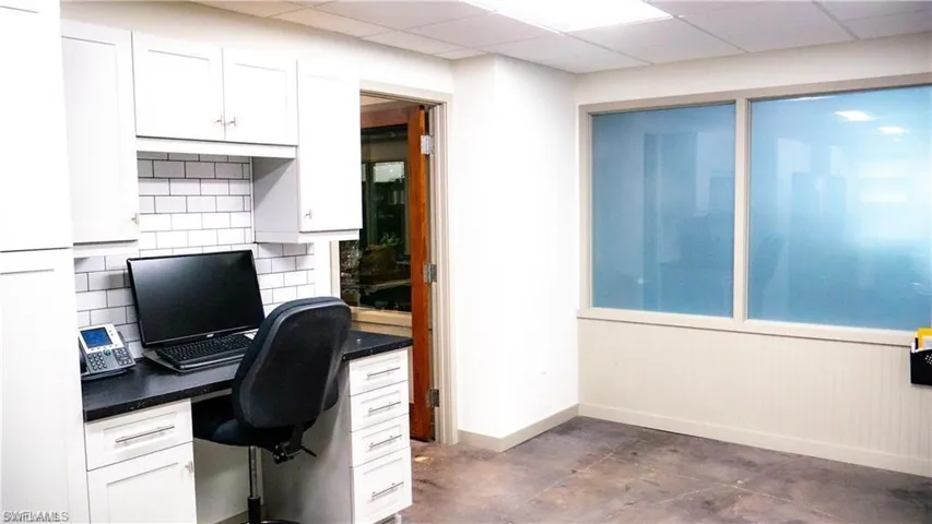Office featuring a paneled ceiling, baseboards, concrete flooring, and built in desk