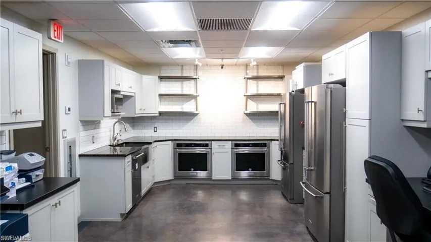 Kitchen featuring dark countertops, a sink, appliances with stainless steel finishes, and open shelves