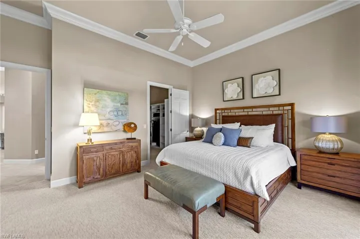 Bedroom featuring a spacious walk in closet, crown molding, light colored carpet, and a ceiling fan