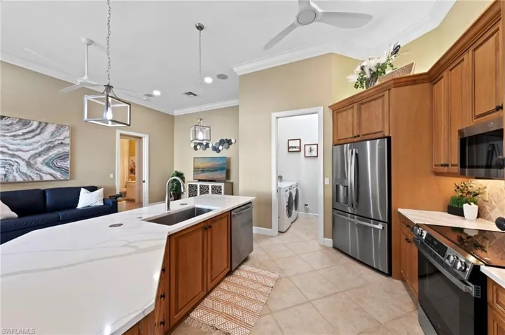 Kitchen with brown cabinets, stainless steel appliances, crown molding, hanging light fixtures, and open floor plan