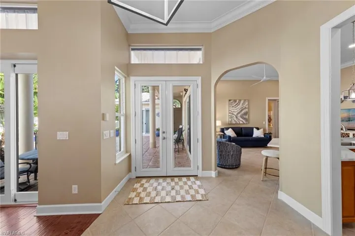 Foyer with french doors, arched walkways, crown molding, and light tile patterned floors