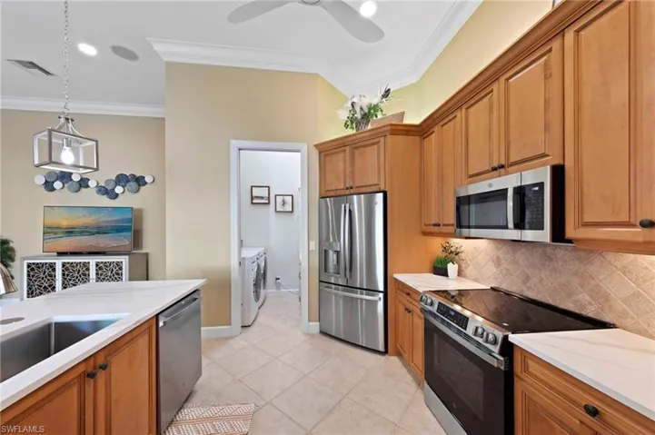 Kitchen with stainless steel appliances, brown cabinetry, crown molding, pendant lighting, and tasteful backsplash