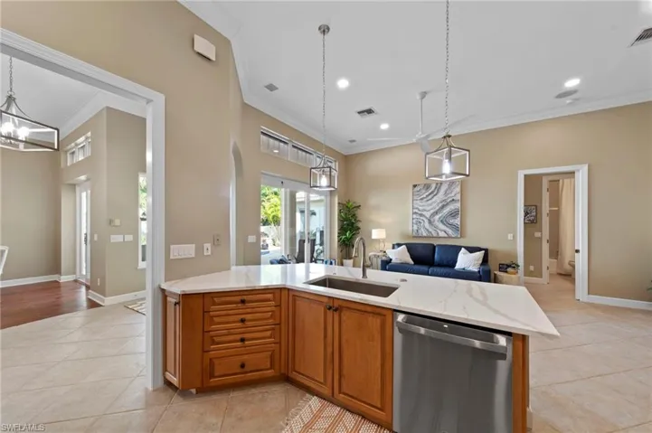 Kitchen featuring brown cabinets, open floor plan, stainless steel dishwasher, hanging light fixtures, and light  countertops