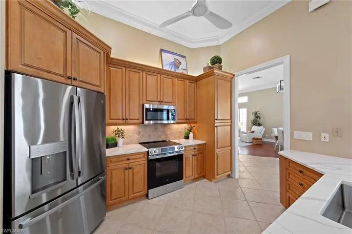 Kitchen with appliances with stainless steel finishes, ornamental molding, light tile patterned flooring, brown cabinetry, and backsplash