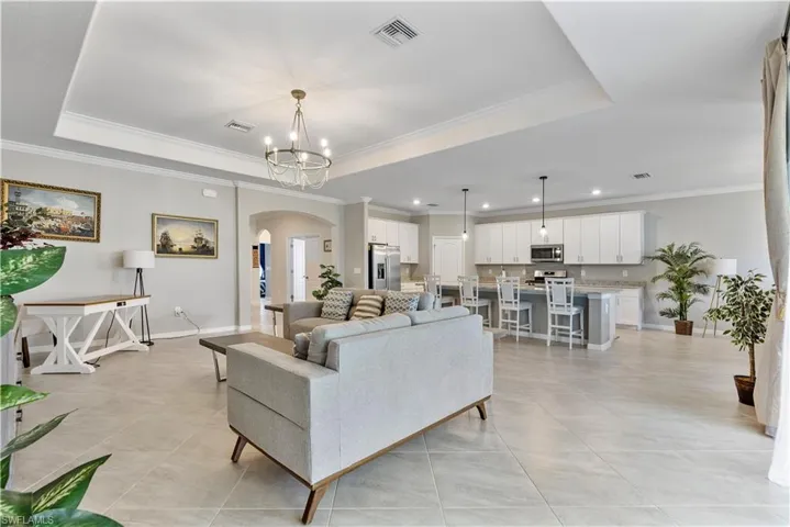 Tiled living room featuring an inviting chandelier, a tray ceiling, and ornamental molding