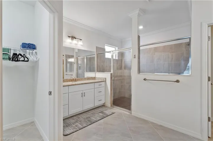 Bathroom with crown molding, vanity, tile patterned floors, and a shower with shower door